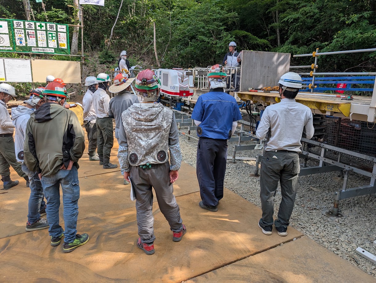 「安全第一」の掲示板の前で講師の説明を聞く、モノレール講習会の参加者
